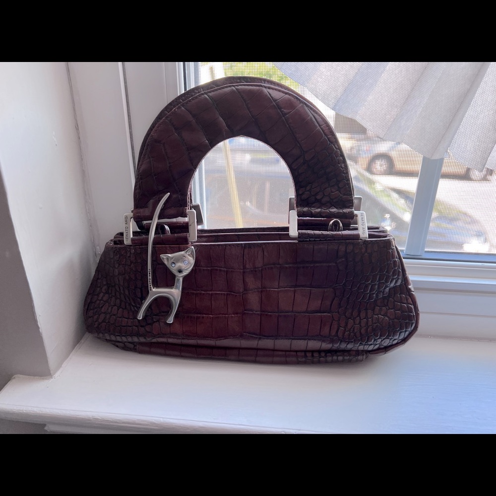 A brownish handbag with a cat pin on it